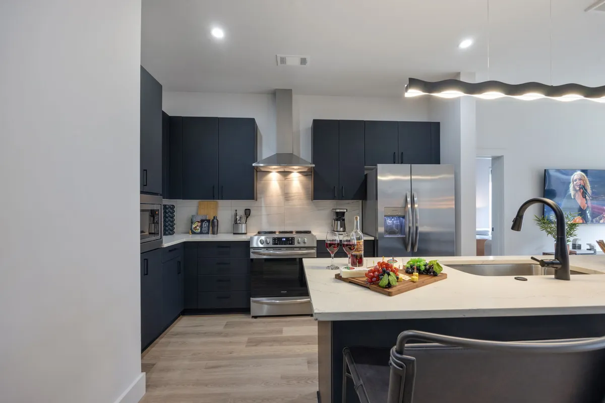 This image highlights a kitchen island set for entertaining, complete with a chopping board laden with food and wine glasses ready for guests. Stainless steel appliances in the background reinforce the kitchen's modern functionality, while the setup captures the spirit of preparing and enjoying meals together.