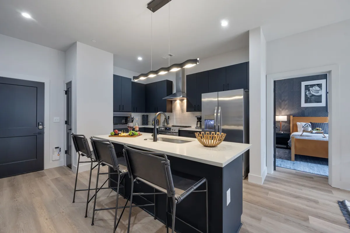 A chic interior shot showcasing a kitchen island, gleaming stainless steel appliances, bar stools lined up for casual dining, and a fresh fruit arrangement. The space exudes a warm, inviting ambiance, perfect for both meal preparation and entertaining guests.