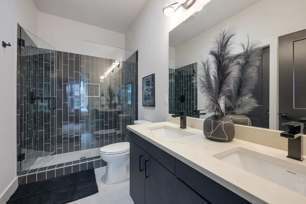 A contemporary bathroom featuring a glass shower enclosure, dual sinks with dark cabinetry, and tasteful decorative accents like a vase. The space exudes modern comfort and tranquility.