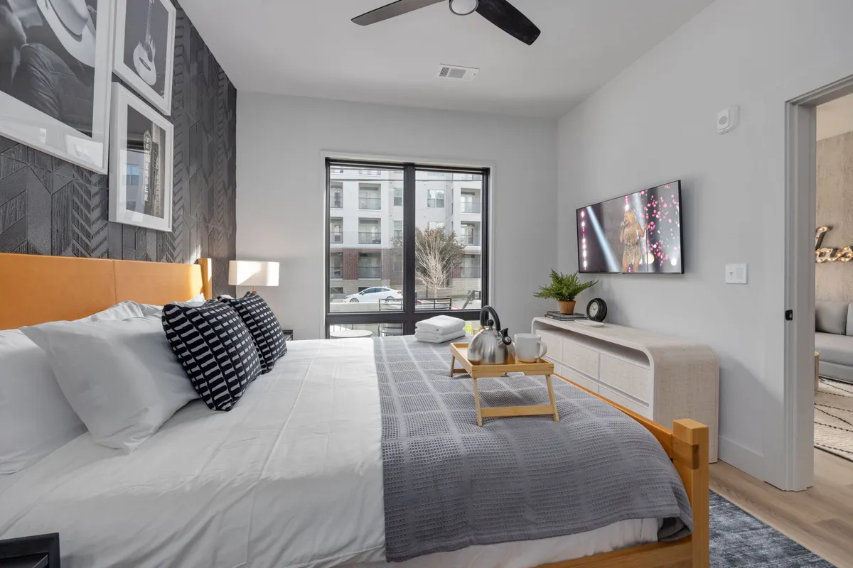 A cozy bedroom with a bed positioned near a window, a TV for entertainment, and decorative touches that make the space feel personal and inviting. Natural light enhances the welcoming mood.