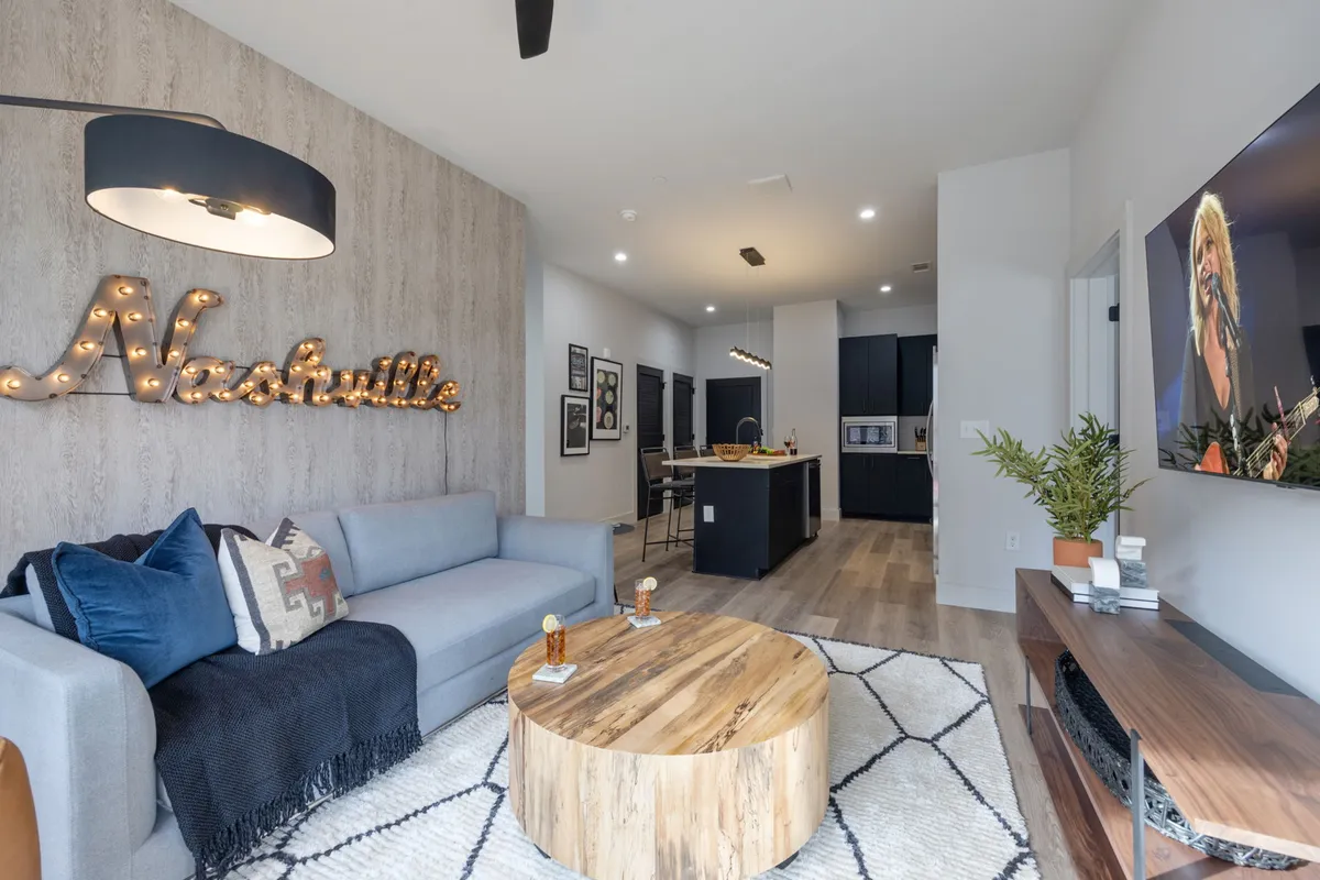 A stylish living room scene featuring a blue couch, iconic Nashville sign, wooden coffee table, wall art, and a large TV display. The decor is music-themed, and the setup is ideal for gatherings, entertainment, and soaking in local culture.