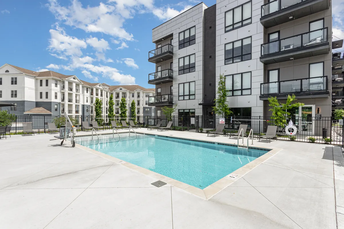 A sunlit swimming pool surrounded by balconies and landscaped trees, suggesting opportunities for poolside gatherings and relaxation. The inviting pool area hints at group BBQs and social events, with the building’s balconies reinforcing the idea of city living and community interaction.